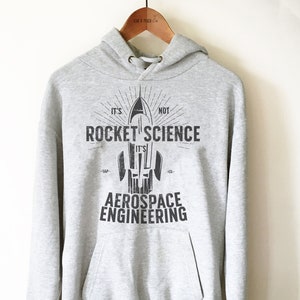 Op de afbeelding: Grijs hoodie met een raketgrafiek en de tekst "Het is geen raketwetenschap, het is lucht- en ruimtevaarttechniek."
