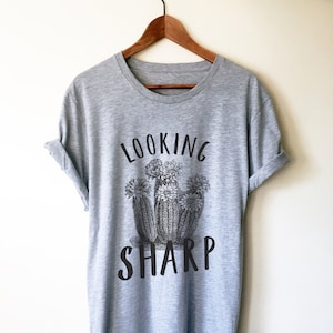 Peut inclure: Un t-shirt gris chiné avec un motif noir de cactus et le texte "LOOKING SHARP".