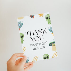 May include: A white thank you card with a green alien, a rocket ship, and a star design. The text on the card reads "Thank You for beaming up to my party from Jack".