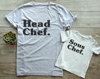 Könnte beinhalten: Zwei graue T-Shirts mit schwarzem Text. Das größere Shirt sagt "Head Chef." Das kleinere Shirt sagt "Sous Chef."