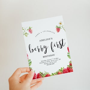 May include: A pink and green invitation card with a strawberry design. The text reads "Come Celebrate Adeline's Berry First Birthday. Saturday August 7, 11-12pm Strawberry Farm, Berry Lane, SD. Regrets only to Lana 888.888.8888"