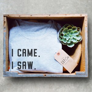 Może przedstawiać: Szary T-shirt z tekstem "I CAME. I SAW." w drewnianej skrzyni z małą sukulentem i brązową etykietą z tekstem "SGP Co."