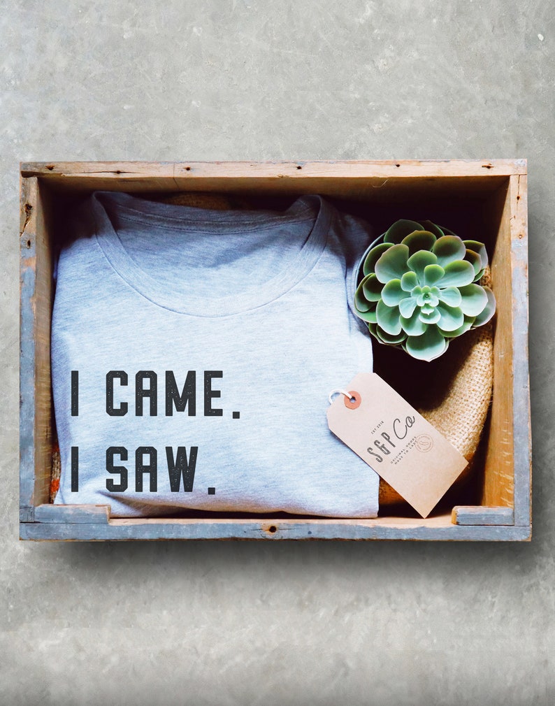 Może przedstawiać: Szary T-shirt z tekstem "I CAME. I SAW." w drewnianej skrzyni z małą sukulentem i brązową etykietą z tekstem "SGP Co."