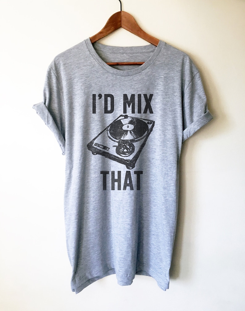 May include: A heather gray t-shirt with the text "I'D MIX THAT" above a black and white illustration of a record player. The shirt is hanging on a wooden hanger.