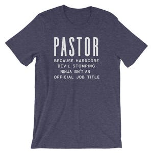 May include: Navy blue t-shirt with white text that reads "PASTOR because hardcore devil stomping ninja isn't an official job title".