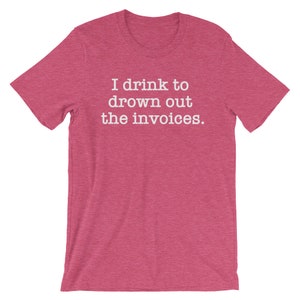 Puede incluir: Una camiseta de color rosa claro con el texto "I drink to drown out the invoices." impreso en blanco.