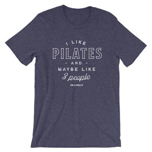 Pode incluir: Uma camiseta azul escura com texto branco que diz "Eu gosto de Pilates - e - talvez como 3 pessoas" e o logotipo "Stag & Peach Co."
