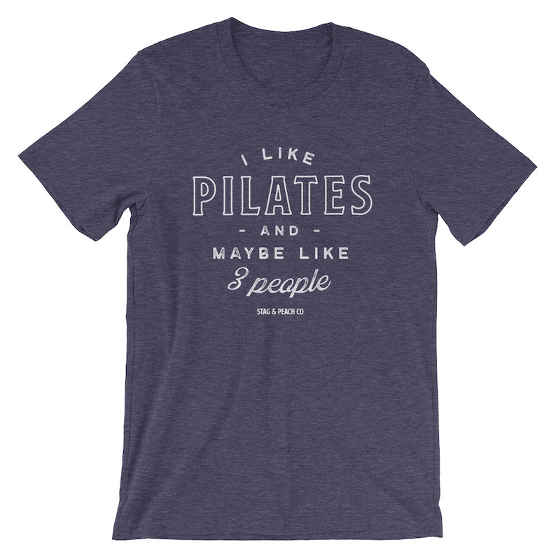 Pode incluir: Uma camiseta azul escura com texto branco que diz "Eu gosto de Pilates - e - talvez como 3 pessoas" e o logotipo "Stag & Peach Co."
