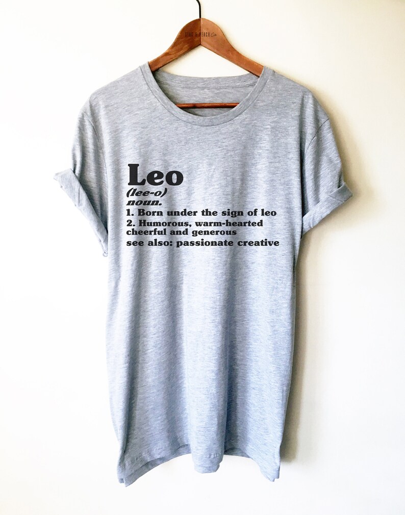 May include: Gray t-shirt with black text that reads "Leo (lee-o) noun. 1. Born under the sign of leo 2. Humorous, warm-hearted cheerful and generous see also: passionate creative"