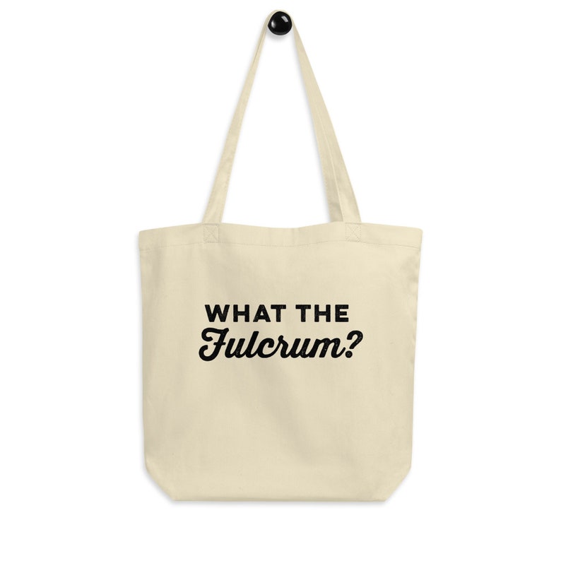 May include: A beige tote bag with black text that reads "WHAT THE FULCRUM?"