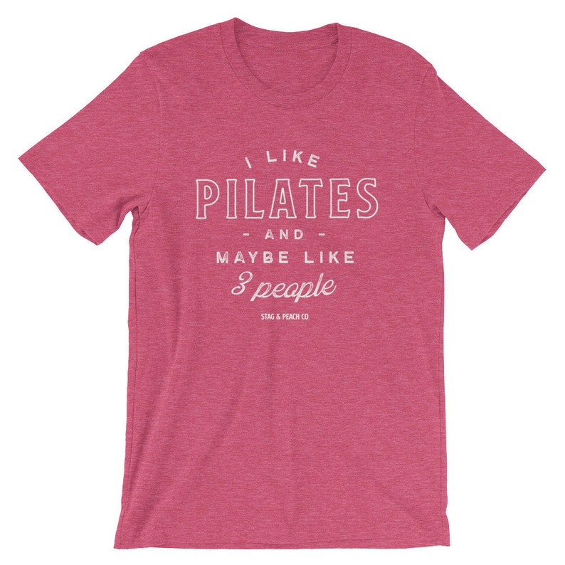 Pode incluir: Uma camiseta rosa heather com texto branco que diz "Eu gosto de Pilates - e - talvez como 3 pessoas" e "Stag & Peach Co."