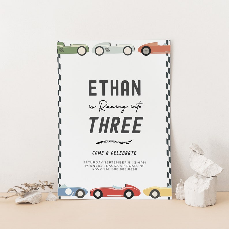 May include: A white and black chequered race track border surrounds a birthday party invitation for Ethan's third birthday. The invitation features a red, white, and blue racing car with the text "Ethan is Racing into Three" and "Come & Celebrate" with the date, time, and location of the party.