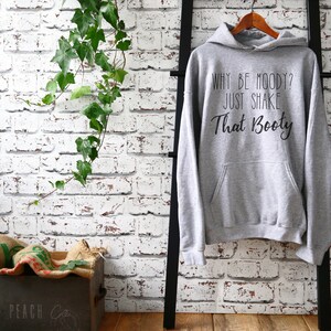 May include: Gray hooded sweatshirt with the text "Why be moody? Just shake that booty" printed on the front.