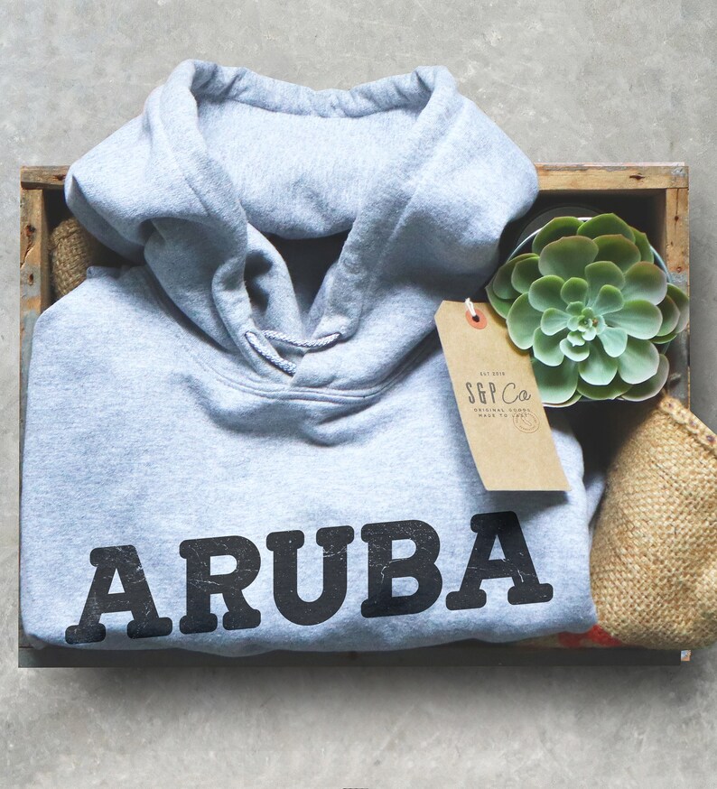 Pu&ograve; includere: Una felpa grigia con la parola "ARUBA" stampata in nero sul davanti. La felpa &egrave; in una cassa di legno con una piccola pianta grassa e un'etichetta marrone che dice "S&P Co. Original Goods Made to Last".