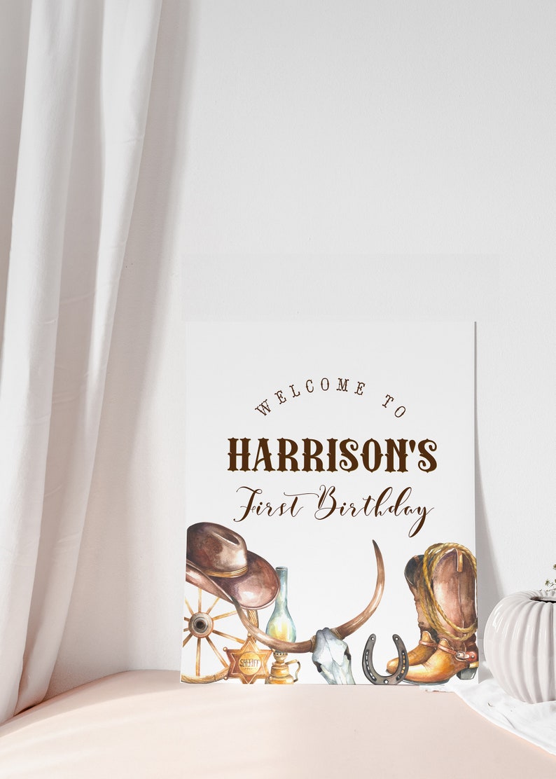 Może przedstawiać: Biały znak z brązowym tekstem, na kt&oacute;rym widnieje napis "Welcome to Harrison's First Birthday". Znak jest ozdobiony kowbojskim kapeluszem, butami, podkową, czaszką i kołem od wozu.
