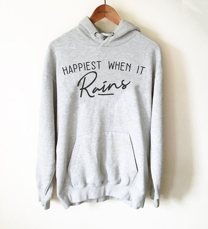 Puede incluir: Una sudadera con capucha gris con el texto "Happiest When It Rains" en letra negra.