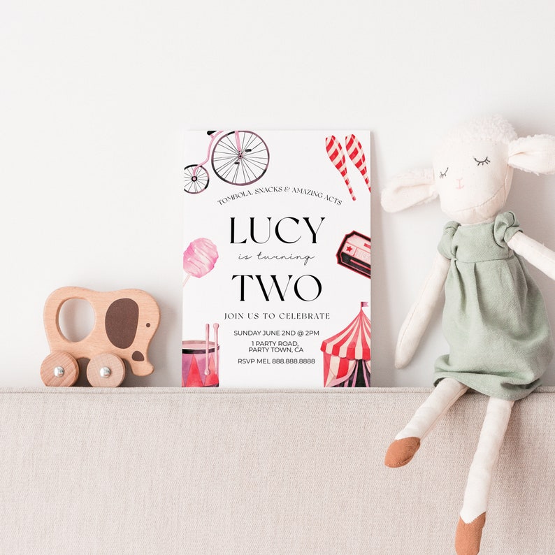 May include: A pink and white birthday invitation for a girl turning two. The invitation features a circus theme with a red and white striped tent, a pink cotton candy, a red and white striped lollipop, a red and white striped drum, and a vintage bicycle. The text on the invitation reads "Lucy is turning two. Join us to celebrate Sunday June 2nd at 2pm, 1 Party Road, Party Town, CA. RSVP Mel 888.888.8888."