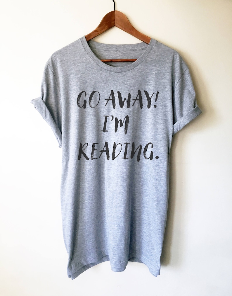 Puede incluir: Una camiseta gris con el texto "GO AWAY! I'M READING." impreso en negro.