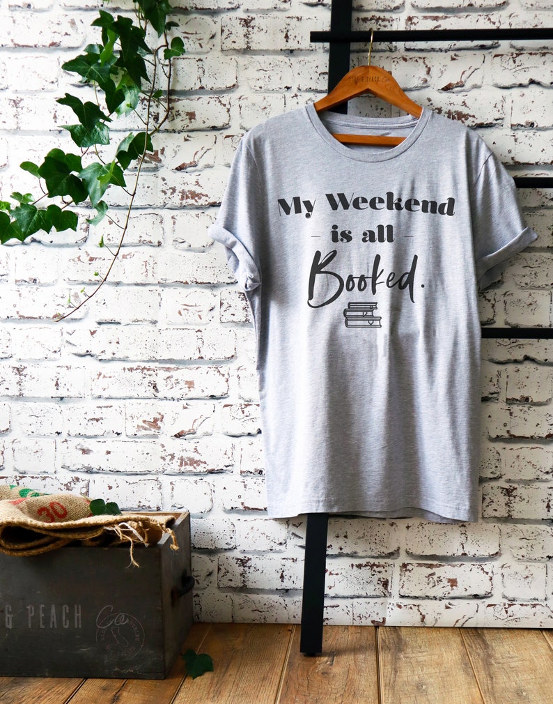 May include: A gray t-shirt with the text "My Weekend is all Booked." in black lettering. The text is stylized with a stack of books underneath the word "Booked."