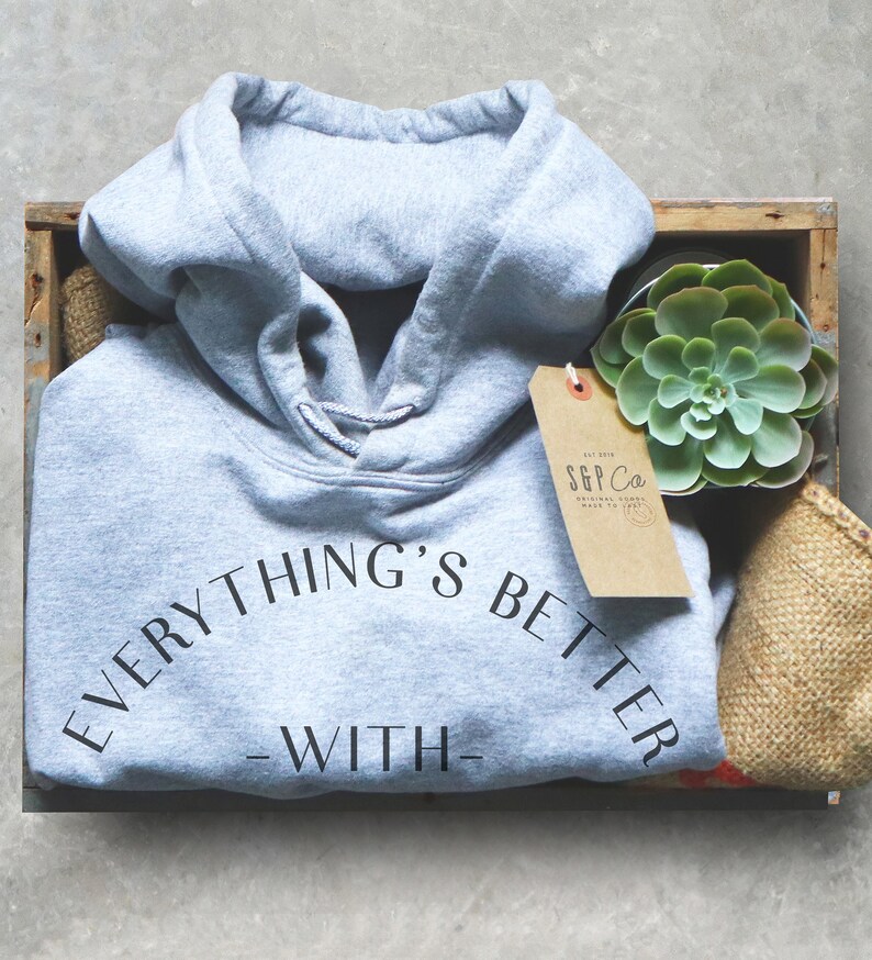 May include: A gray hooded sweatshirt with the text "EVERYTHING'S BETTER - WITH -" printed on the front. The sweatshirt is in a wooden crate with a small potted succulent plant and a brown paper tag with the text "S&P Co. ORIGINAL GOODS MADE TO LAST" printed on it.