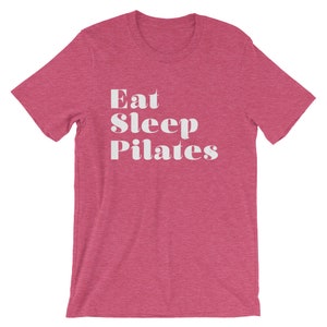 Pode incluir: Uma camiseta rosa claro com o texto "Eat Sleep Pilates" em branco.