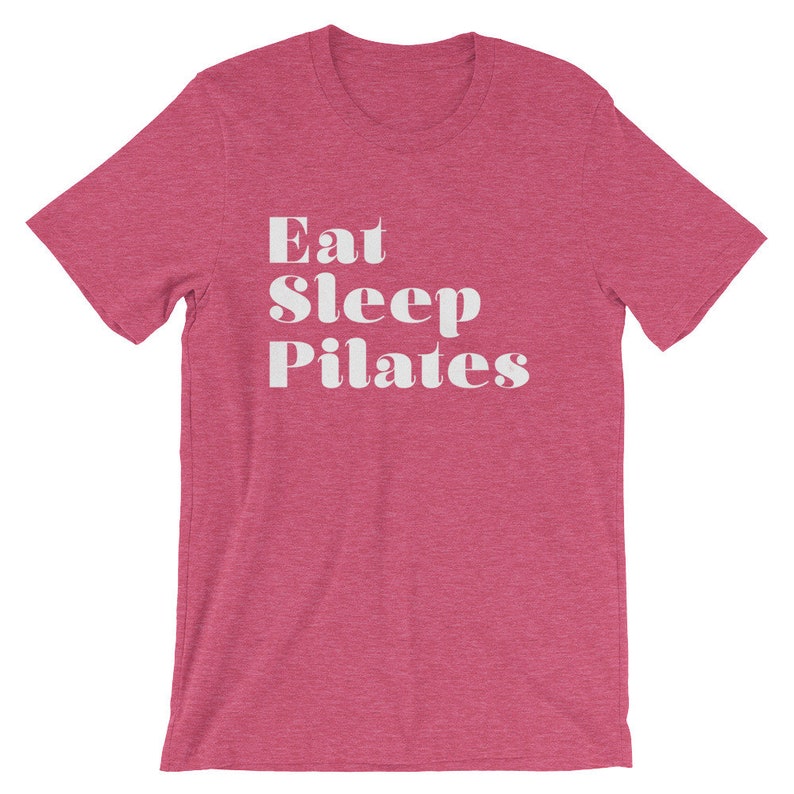 Pode incluir: Uma camiseta rosa claro com o texto "Eat Sleep Pilates" em branco.
