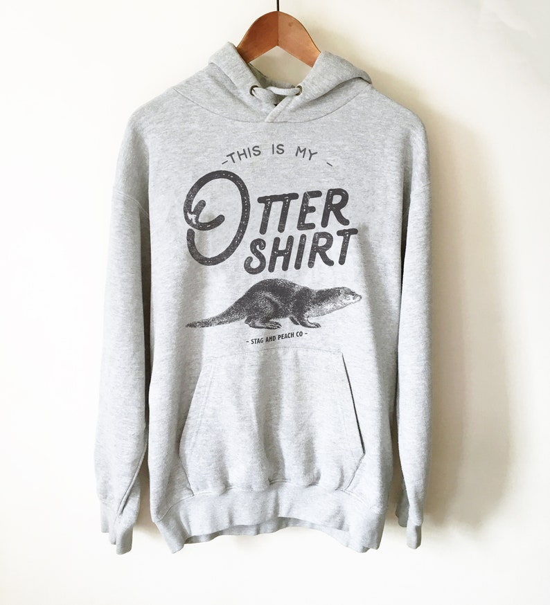 Puede incluir: Sudadera gris con capucha con un gr&aacute;fico de una nutria y el texto "This is my Otter Shirt - Stag and Peach Co."