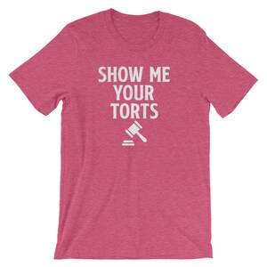 May include: A pink t-shirt with the text "SHOW ME YOUR TORTS" in white lettering and a white gavel icon.