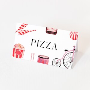 May include: A white card with red and white circus-themed illustrations, including a popcorn bucket, a drum, a unicycle, and a striped tent. The text "PIZZA" is printed in black on the card.