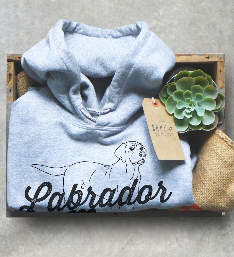 May include: A light grey hooded sweatshirt with a black outline of a Labrador Retriever and the text "Labrador" in a black vintage-style font.
