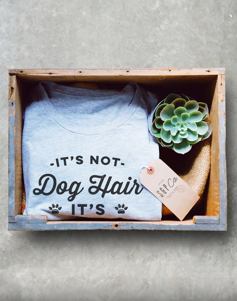 May include: A gray t-shirt with the text "It's not Dog Hair It's" and paw prints. The t-shirt is in a wooden crate with a small succulent plant and a brown tag with the text "SFF Co."