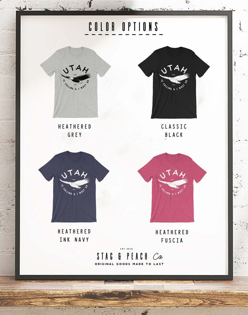 Op de afbeelding: Vier T-shirts in verschillende kleuren: grijs melange, klassiek zwart, donkerblauw melange en fuchsia melange. Elk T-shirt heeft een witte afbeelding van een adelaar met de tekst "UTAH IT'S CALLING & I MUST GO". De T-shirts worden weergegeven op een witte achtergrond met de tekst "COLOR OPTIONS" bovenaan en "STAG & PEACH Co ORIGINAL GOODS MADE TO LAST" onderaan.