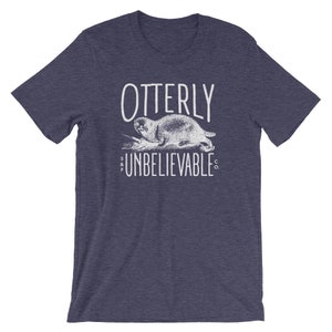 Puede incluir: Una camiseta azul marino con un gr&aacute;fico blanco de una nutria y el texto "Otterly Unbelievable Co."