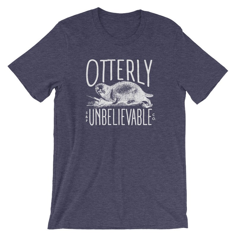 Puede incluir: Una camiseta azul marino con un gr&aacute;fico blanco de una nutria y el texto "Otterly Unbelievable Co."