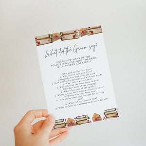 May include: A printable game card with the text "What did the Groom say?" and a list of questions for a bridal shower game. The card is decorated with a watercolor illustration of stacked books and roses.