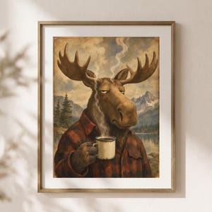 Könnte beinhalten: Ein gerahmter Kunstdruck mit der Illustration eines Elches, der ein rot-schwarz kariertes Flanellhemd trägt. Der Elch hält eine dampfende weiße Tasse. Der Hintergrund zeigt eine Berglandschaft mit einem See, Tannen und einem bewölkten Himmel.