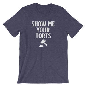 May include: A navy blue t-shirt with the text "Show Me Your Torts" in white lettering. A white gavel icon is below the text.
