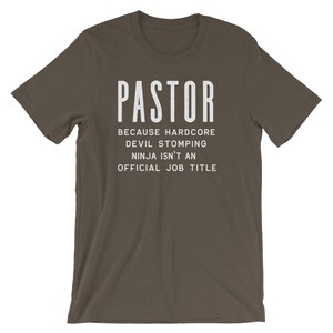 May include: A dark brown t-shirt with the text "PASTOR" in white, followed by the text "Because hardcore devil stomping ninja isn't an official job title".