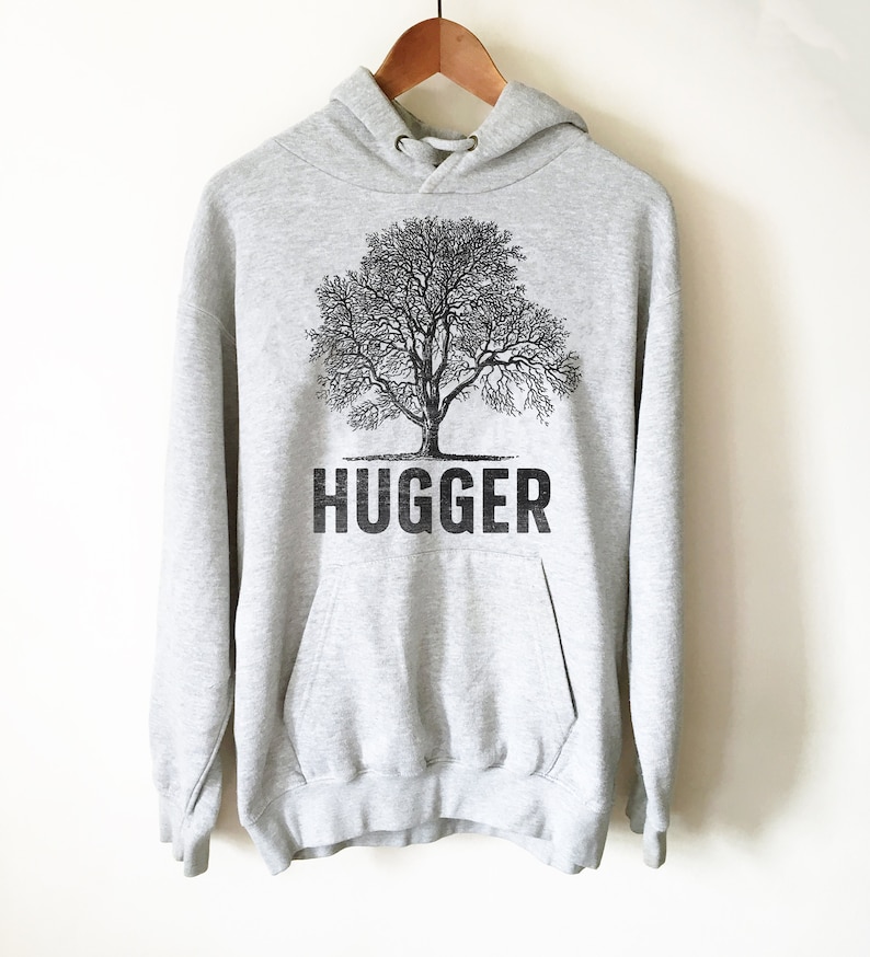 Puede incluir: Una sudadera con capucha gris con un gr&aacute;fico de &aacute;rbol negro y la palabra "HUGGER" impresa debajo.