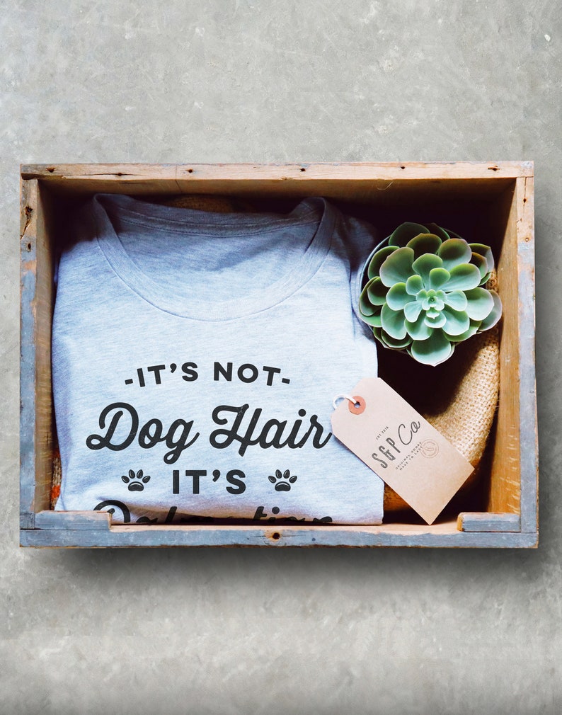 Puede incluir: Una camiseta gris con el texto "It's not Dog Hair It's..." en una caja de madera con una peque&ntilde;a planta suculenta y una etiqueta marr&oacute;n con el texto "SFF Co."