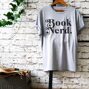 May include: Gray t-shirt with the text "Book Nerd." printed in black with a decorative font.