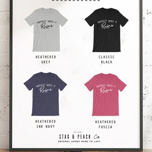 May include: Four t-shirts with the text "Happiest When It Rains" in a white cursive font. The t-shirts are shown in four different colors: heather grey, classic black, heather ink navy, and heather fuscia. The text "Stag & Peach Co. Original Goods Made To Last" is at the bottom of the image.