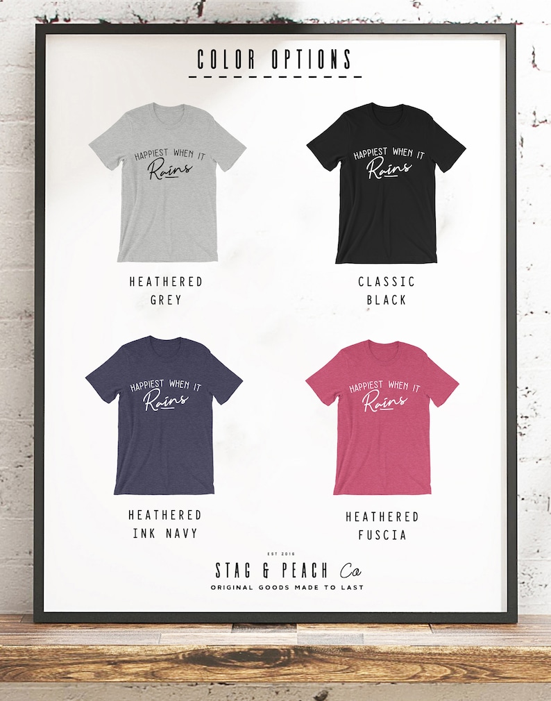 May include: Four t-shirts with the text "Happiest When It Rains" in a white cursive font. The t-shirts are shown in four different colors: heather grey, classic black, heather ink navy, and heather fuscia. The text "Stag & Peach Co. Original Goods Made To Last" is at the bottom of the image.