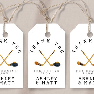 May include: Three white gift tags with black text and a hockey stick and puck design. The text reads "Thank You" and "For Coming From Ashley & Matt".