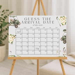 May include: A white baby shower calendar on an easel with the text "GUESS THE ARRIVAL DATE of baby smith." The calendar features a golf theme with illustrations of a golf cart, golf clubs, and baby clothes. The calendar grid spans April and May.