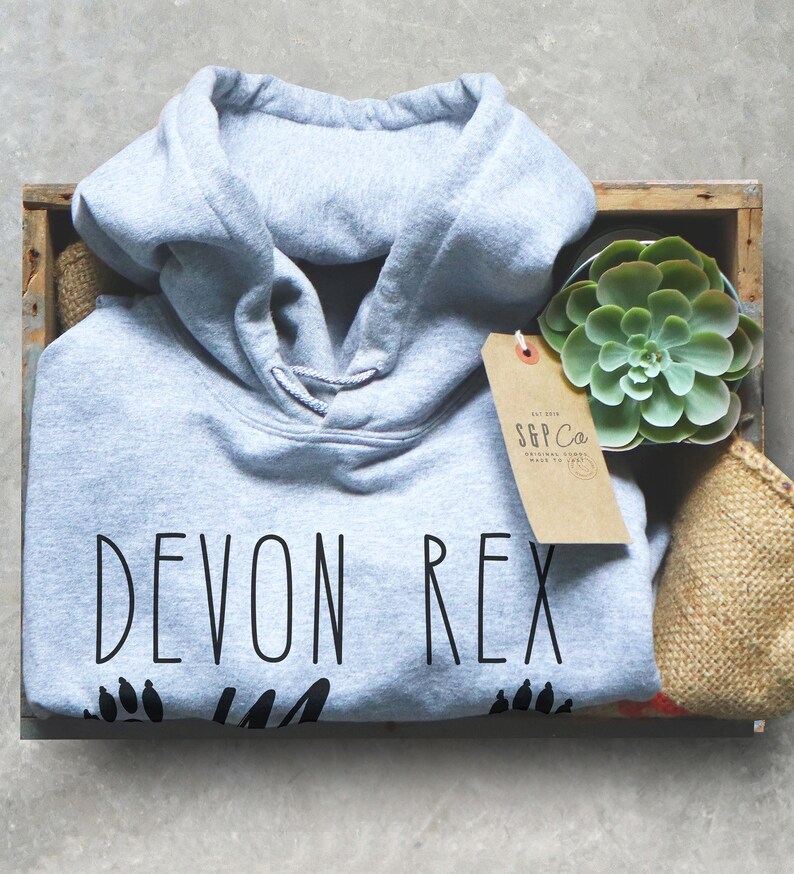 May include: A gray hoodie with the text "DEVON REX" in black, along with paw prints. The hoodie is inside a wooden crate with a succulent plant and a tag that reads "S&P Co. ORIGINAL GOODS MADE TO LAST."