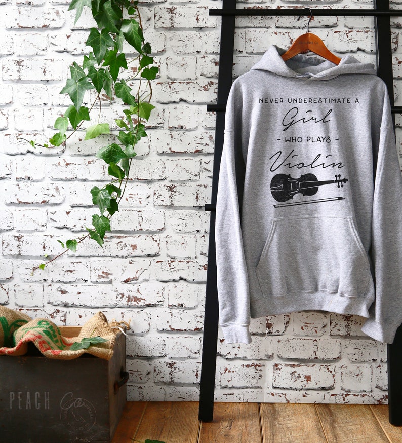 May include: Gray hooded sweatshirt with the text "Never underestimate a girl who plays violin" and a black silhouette of a violin.
