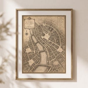 May include: A framed vintage-style map titled Plan du Quartier de Saint-Martin, featuring detailed street layouts, a river, and a legend in the upper right corner. The map is rendered in sepia tones and housed in a thin, metallic gold frame.