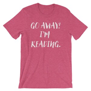 Puede incluir: Una camiseta rosa con el texto "GO AWAY! I'M READING." en blanco.