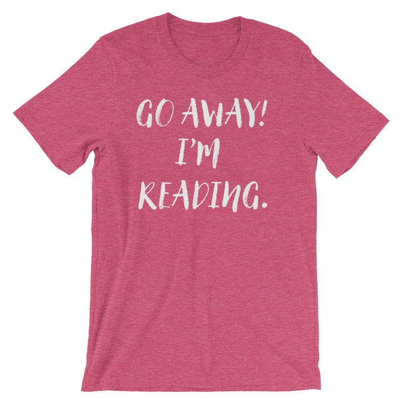Puede incluir: Una camiseta rosa con el texto "GO AWAY! I'M READING." en blanco.